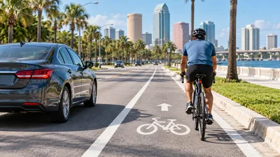 A cyclist rides in a marked Florida bike lane beside a car on a sunny palm-lined roadway.